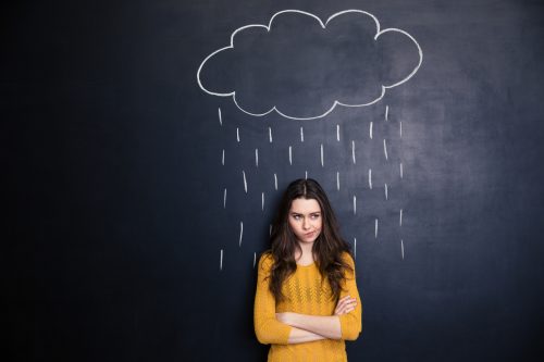 Unpleased woman with raincloud drawn over her on blackboard background